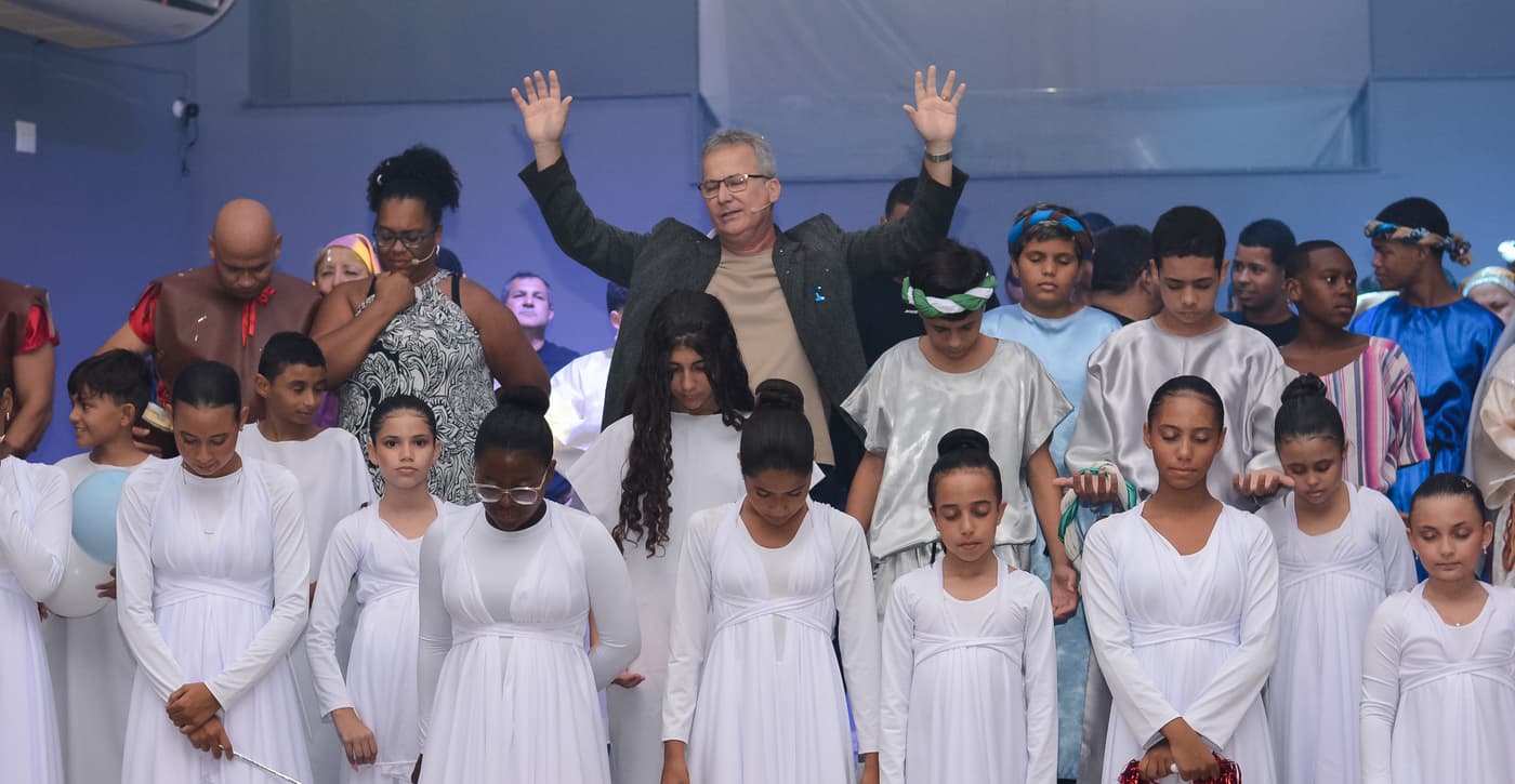 Pastor Liviston abençoando a congregação no palco, com adolescentes do ministério de dança à frente